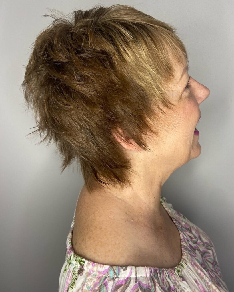 A side profile of a woman over 60 with a sun-kissed caramel bixie cut featuring choppy layers and wispy bangs.