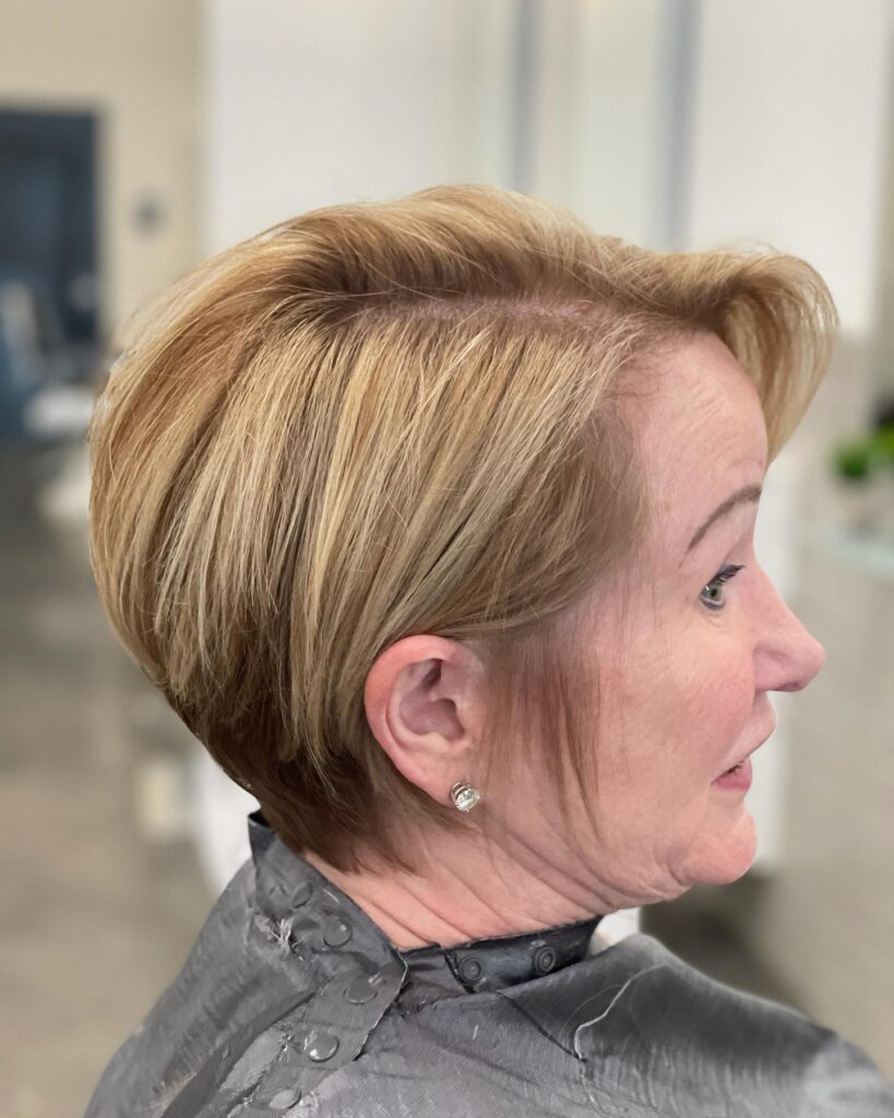 A side profile of a woman over 60 with an elegant strawberry blonde wedge bob featuring a voluminous back and tucked layers.