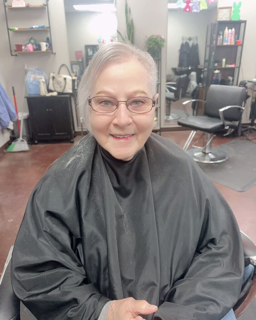 A woman over 60 with a soft, pearly silver pixie cut featuring smooth side-swept layers and a polished finish.