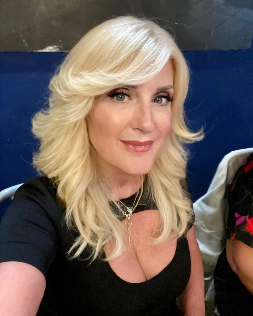 A woman with shoulder-length platinum blonde hair featuring voluminous layers and a side-swept fringe.