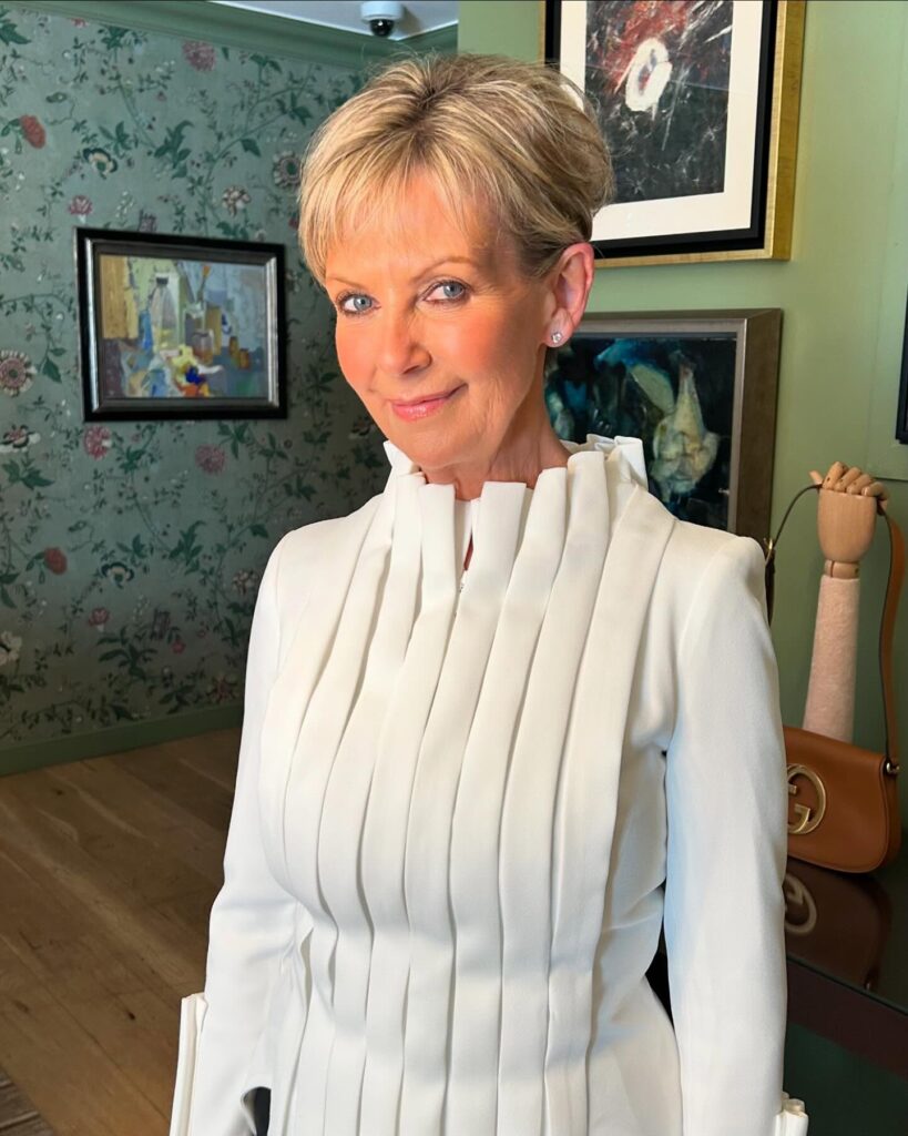 A woman wearing a sophisticated ash blonde pixie cut with fine layers and a soft front fringe.