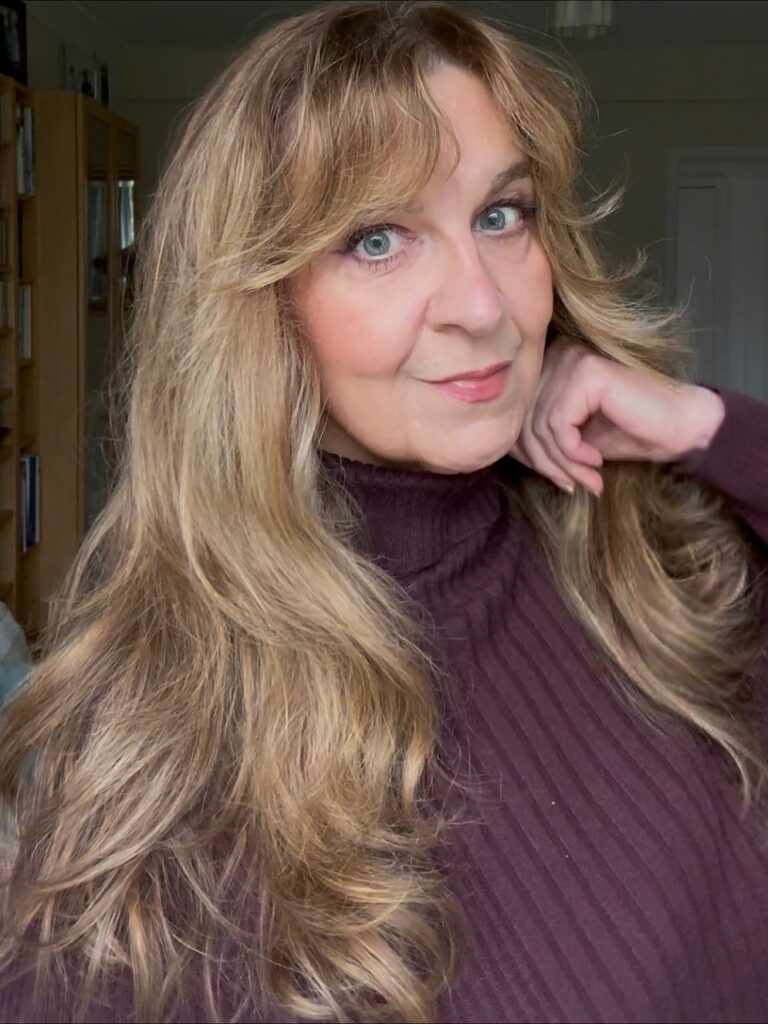 A woman over sixty with long, sandy blonde hair featuring voluminous layers and soft, wispy curtain bangs.