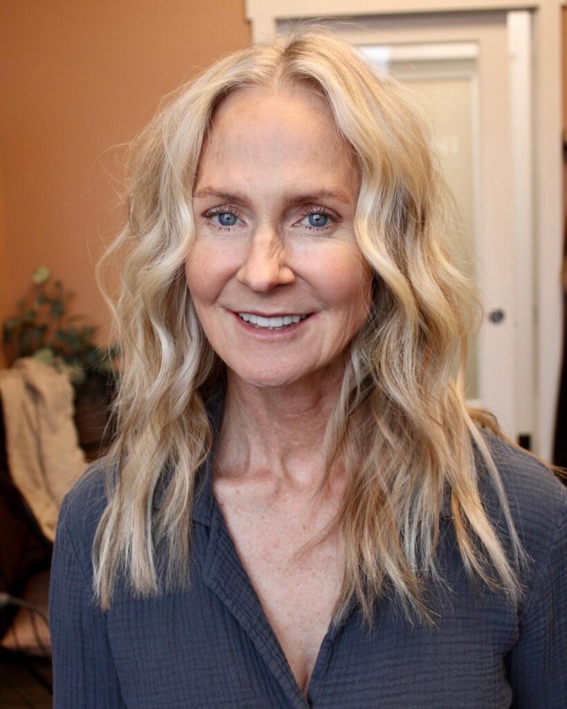 A woman with long sandy blonde hair styled in loose beachy waves with a middle part.