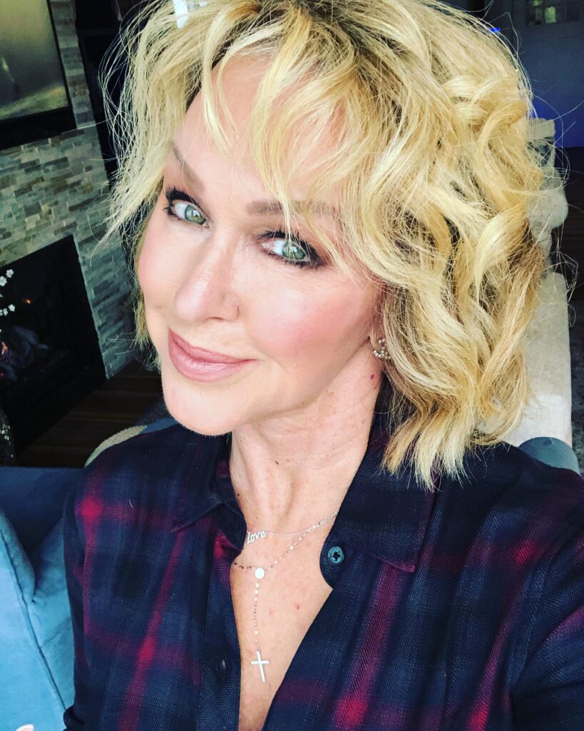 A woman over sixty with a chin-length golden blonde bob featuring bouncy curls and soft wispy bangs.