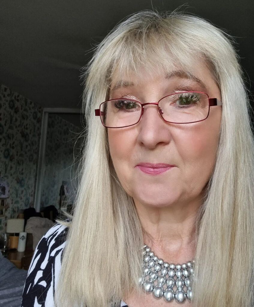 A woman with long, straight, sand-blonde hair and a full fringe wearing red glasses.