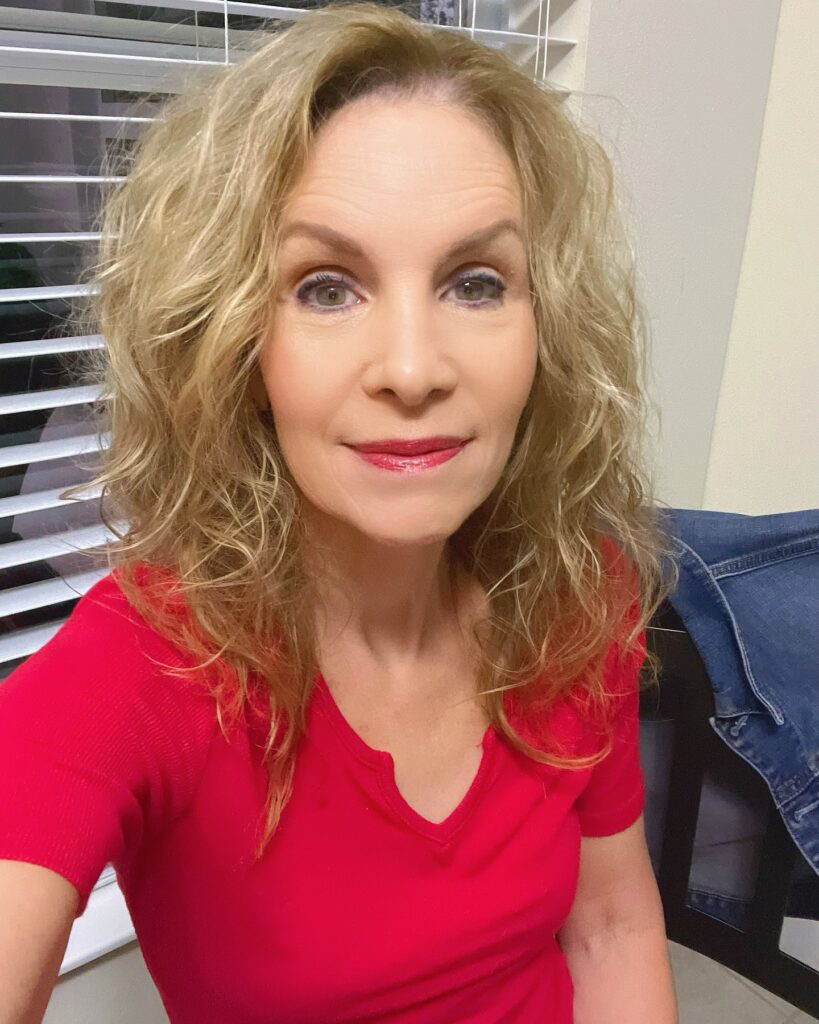 A woman over sixty with shoulder-length curly blonde hair featuring golden highlights and a messy, voluminous style.