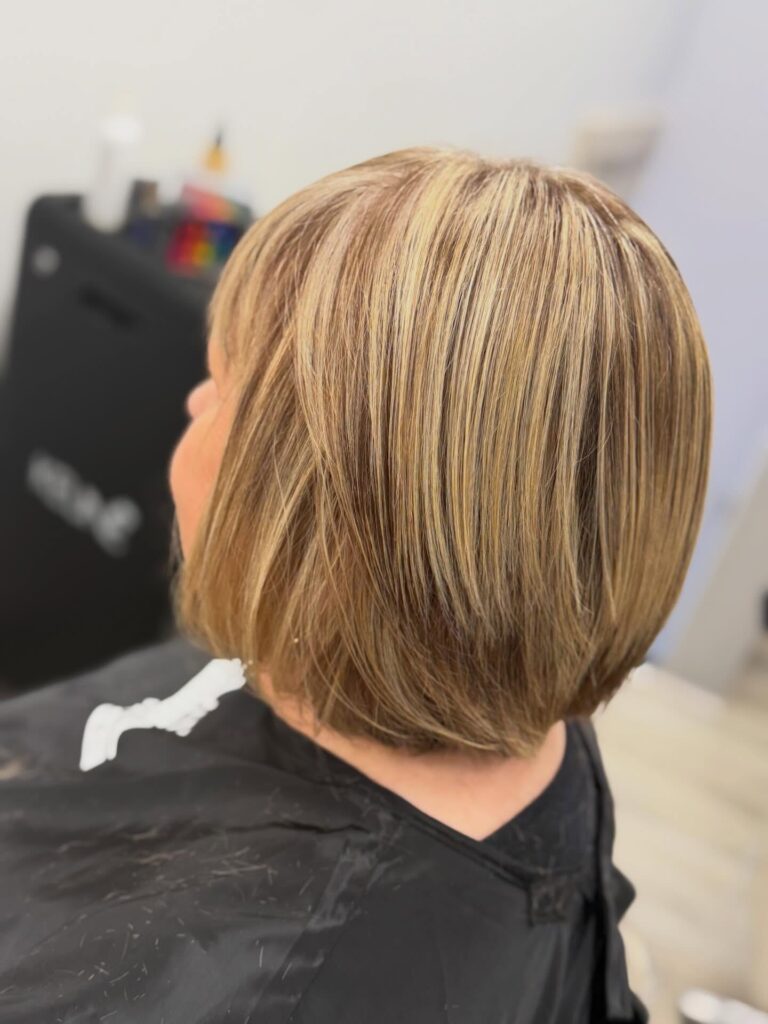 A woman with a chin-length honey blonde bob featuring dimensional highlights and a rounded shape.