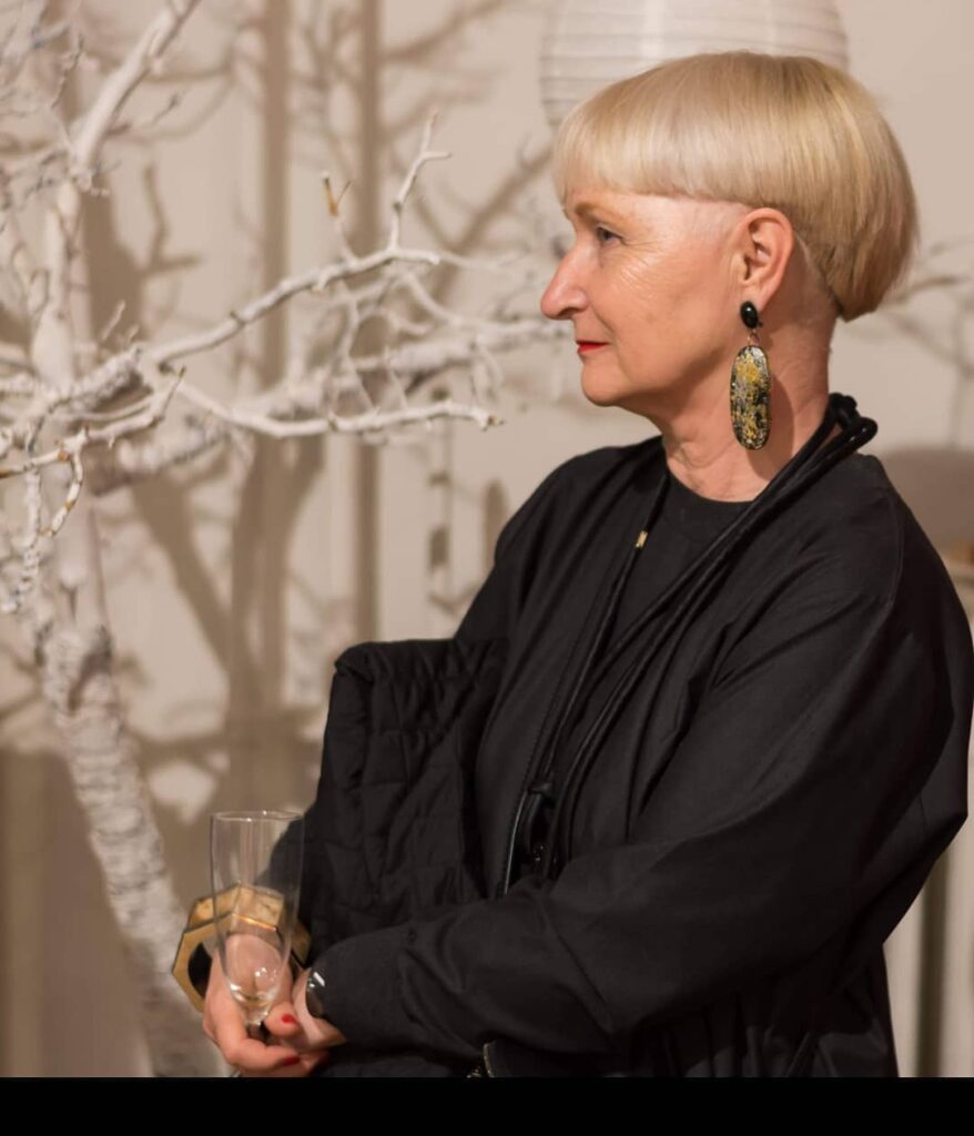 A woman over sixty in profile wearing large earrings and a modern ash-blonde bowl cut with a sharp undercut.