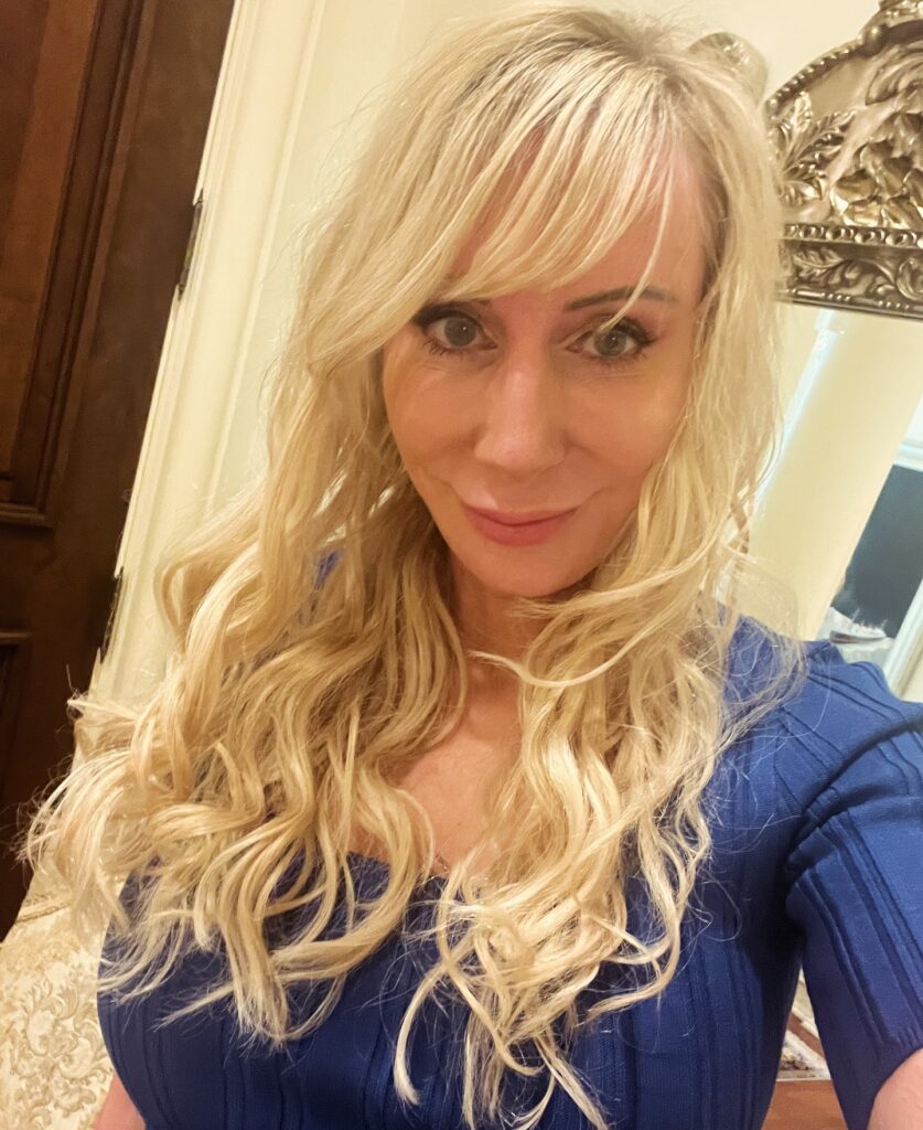 A woman with long, wavy, pale blonde hair and a soft side fringe wearing a blue top.