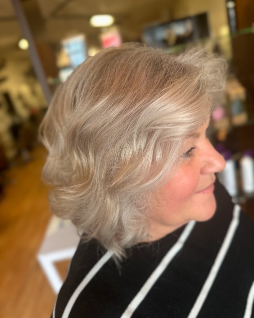 A woman in profile with a wavy neck-length bob in a bright, icy blonde color and lots of volume.