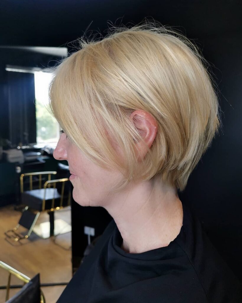 A side profile view of a woman with a short golden blonde bob that is cut slightly shorter in the back with a smooth, straight finish.