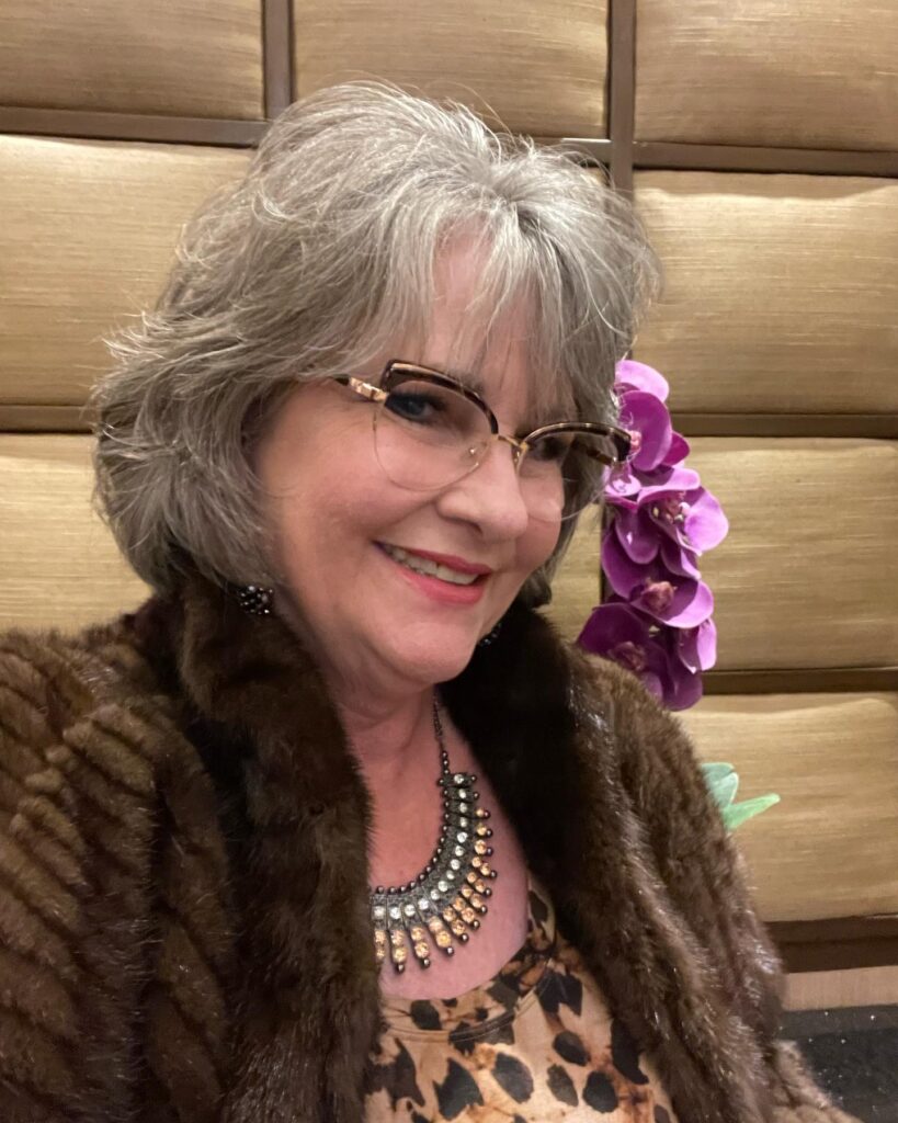 A smiling woman wearing glasses with a chin-length textured grey bob that features soft, wispy bangs and layered ends.