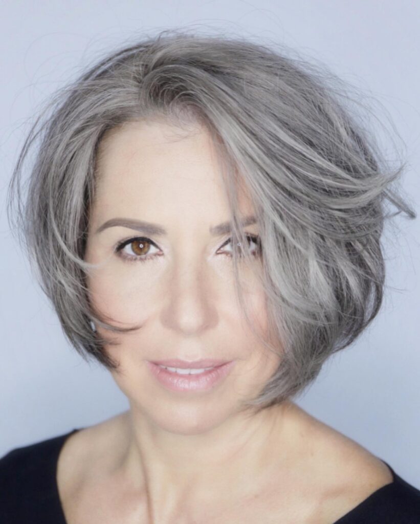 A woman looking forward with an edgy jaw-length asymmetrical silver bob that features a tousled and piecey texture.