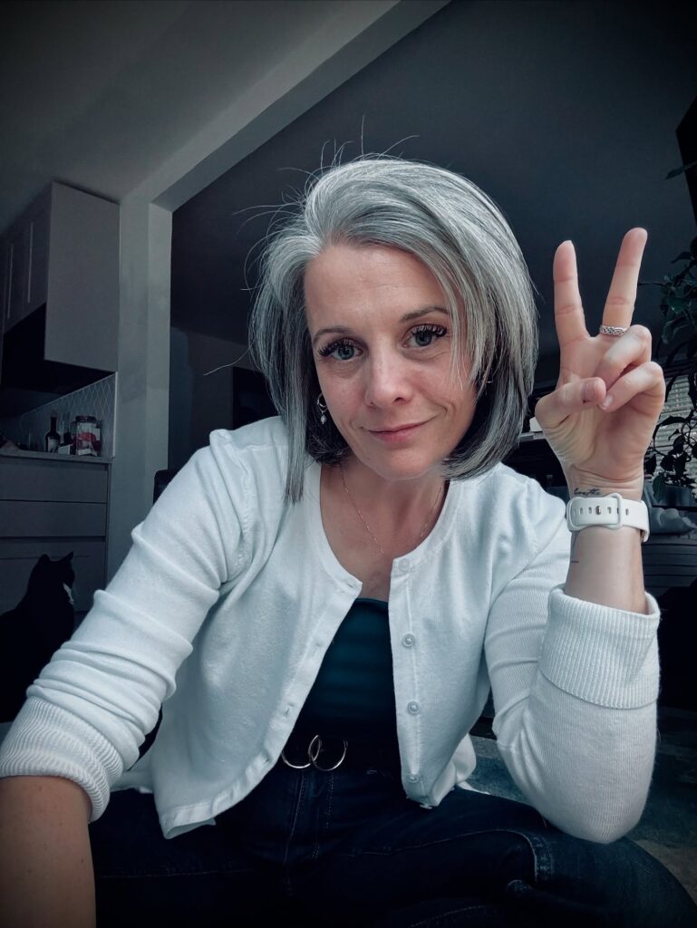 A woman with a sleek chin-length silver bob featuring a deep side part and dark lowlights underneath.