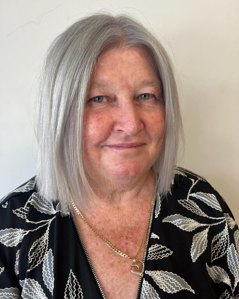 A woman with a straight, shoulder-length icy silver bob featuring a middle part and sleek texture.