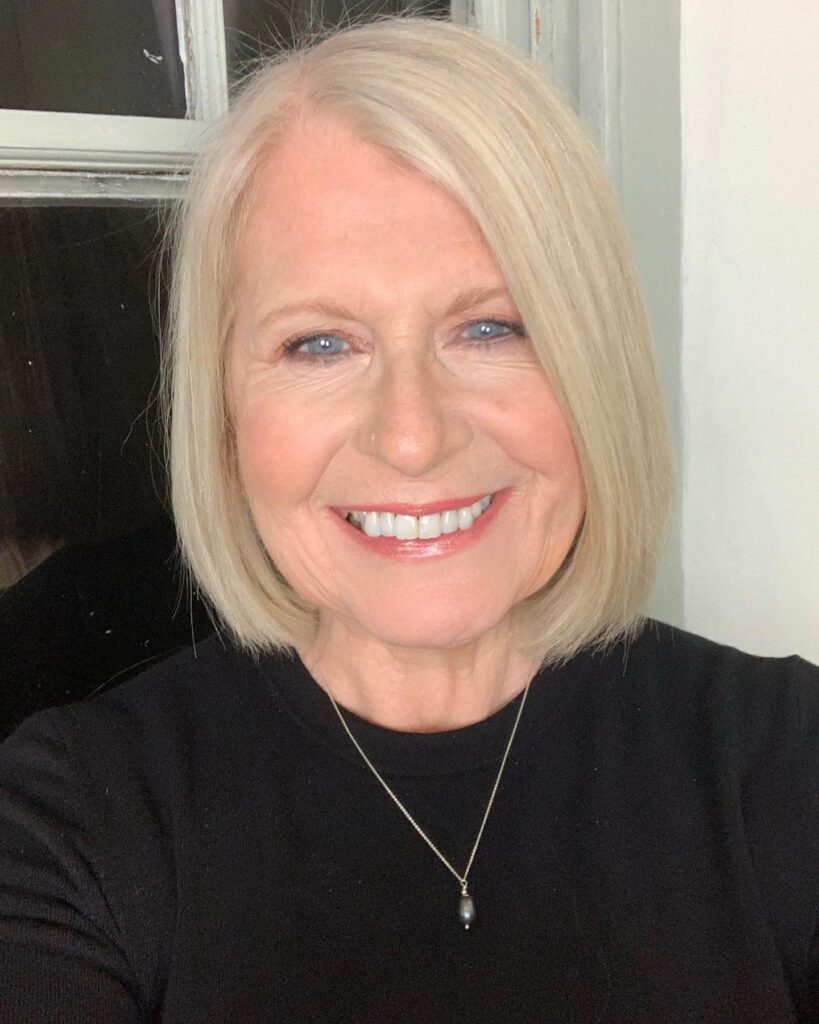 A smiling woman with a sleek, chin-length pale blonde bob featuring a soft side part and smooth texture.