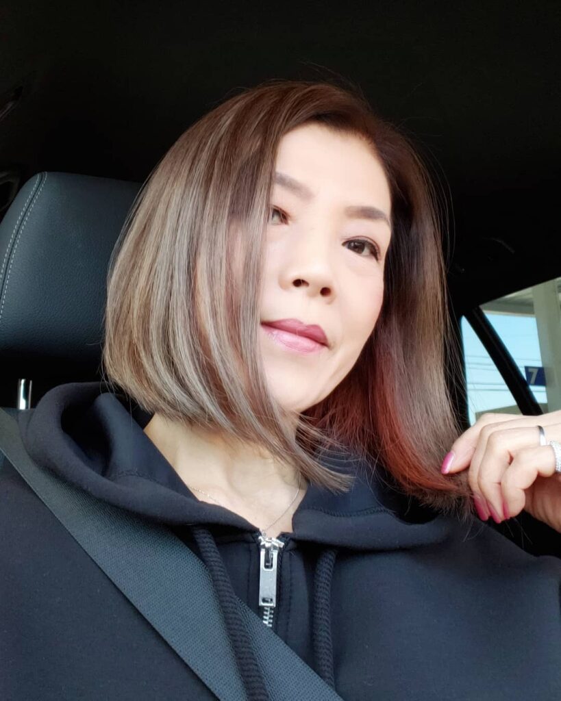 A side profile view of a woman with a chin-length caramel brown bob featuring soft layers and a wispy side-swept fringe.