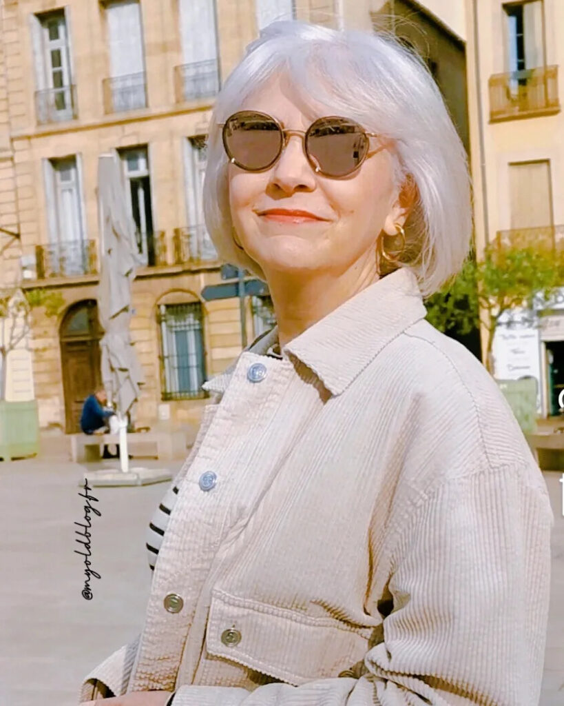 A woman smiling in the sunlight, wearing a breezy, chin-length silver bob with soft layers and a side-swept fringe.