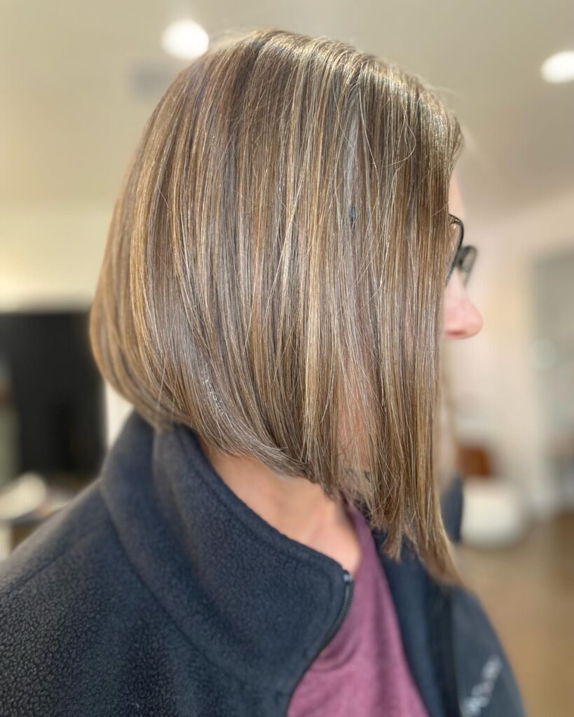 A side profile view of a woman with a sleek, angled ash brown bob featuring fine blonde highlights and a straight texture.