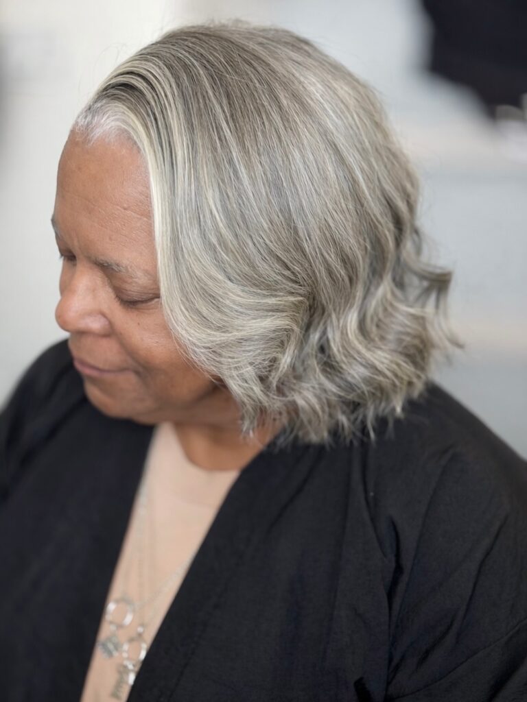 A side and back view of a woman with a stacked, chin-length ash blonde bob featuring textured layers and volume at the crown.