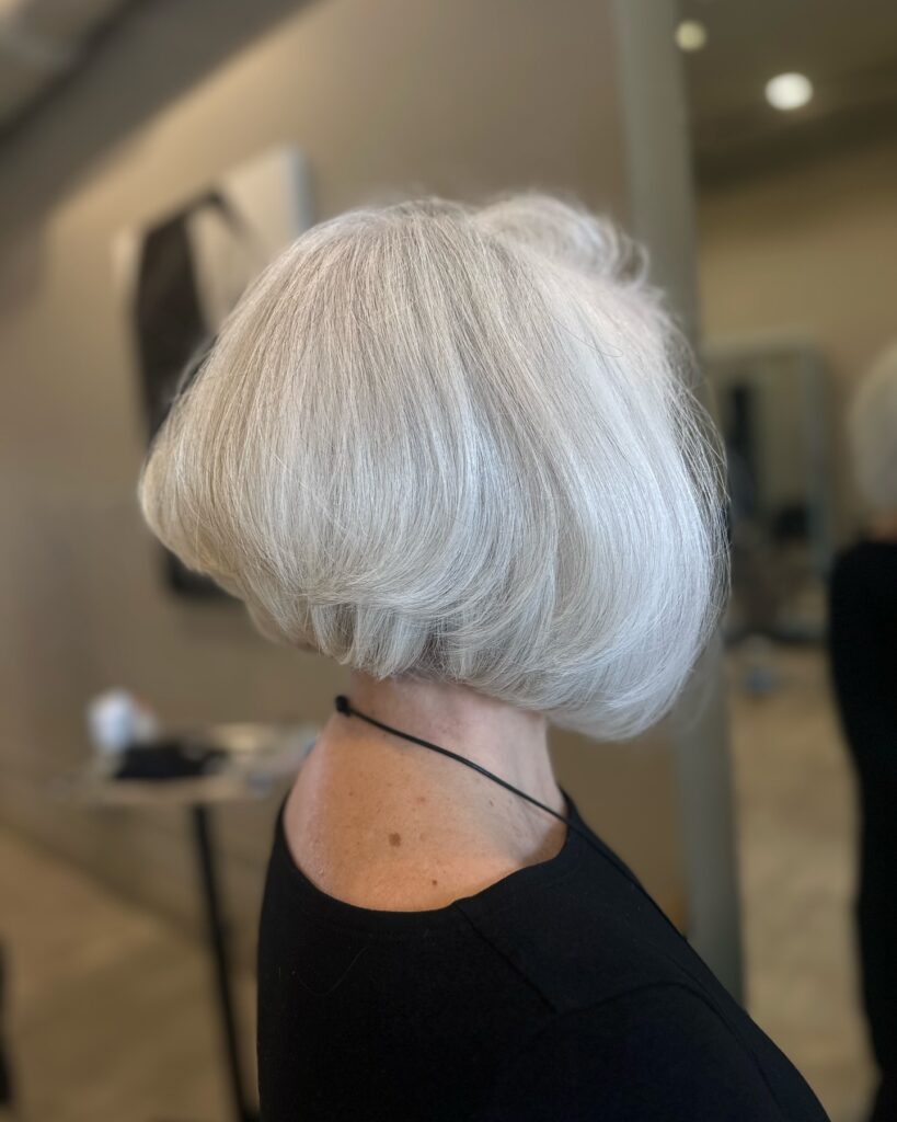 A rear side view of a woman with a sleek, stacked platinum blonde bob featuring dramatic volume at the back and angled sides.