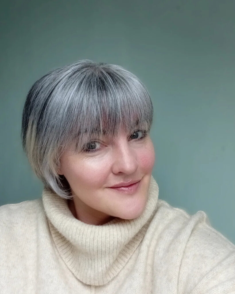 A woman smiling with a short, textured salt and pepper bob that features full, straight-across bangs.