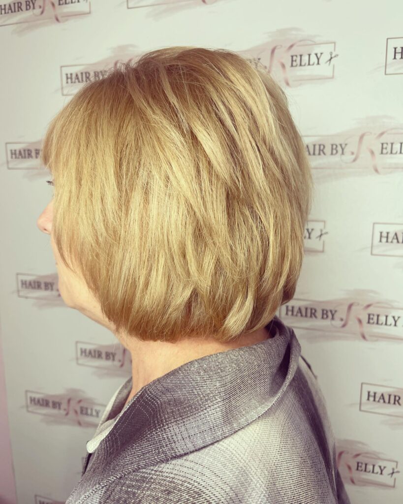 A side profile of a woman with a voluminous honey blonde bob featuring soft, textured layers and gently curved ends.