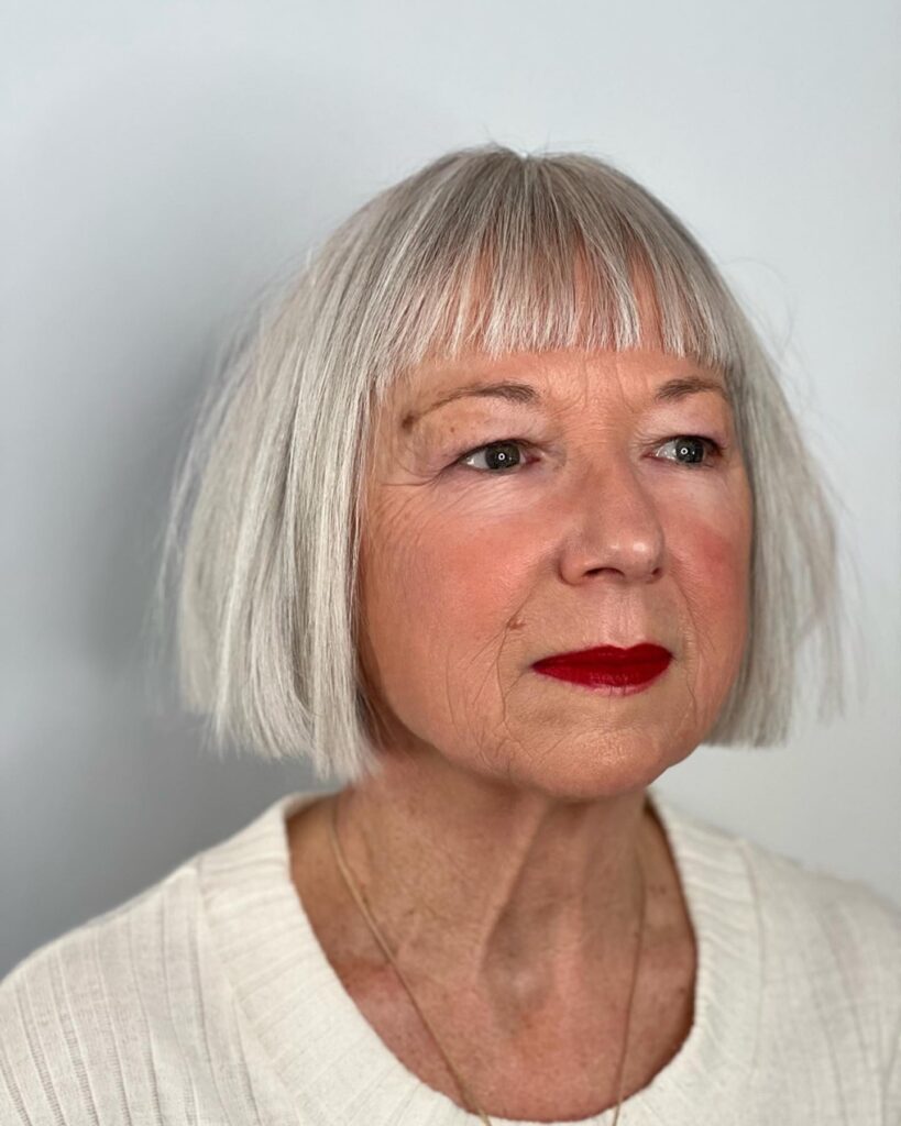 A rear view of a woman with a textured, neck-length silver bob featuring wispy layers and a multidimensional grey color.
