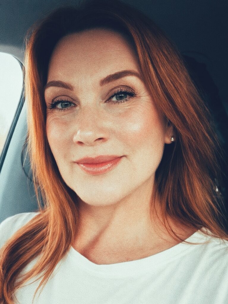 A smiling woman with medium-length layered copper-red hair wearing a white shirt.