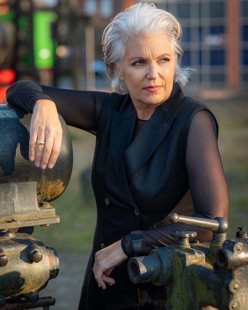 A woman over 60 with a square face wearing a brushed-back silver bixie with tapered sides and textured volume on top.