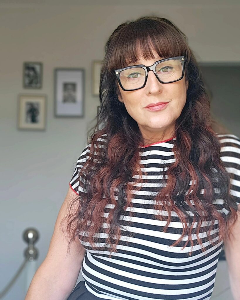 A woman over 60 with a square face wearing long, wavy mahogany hair with a thick, full fringe.