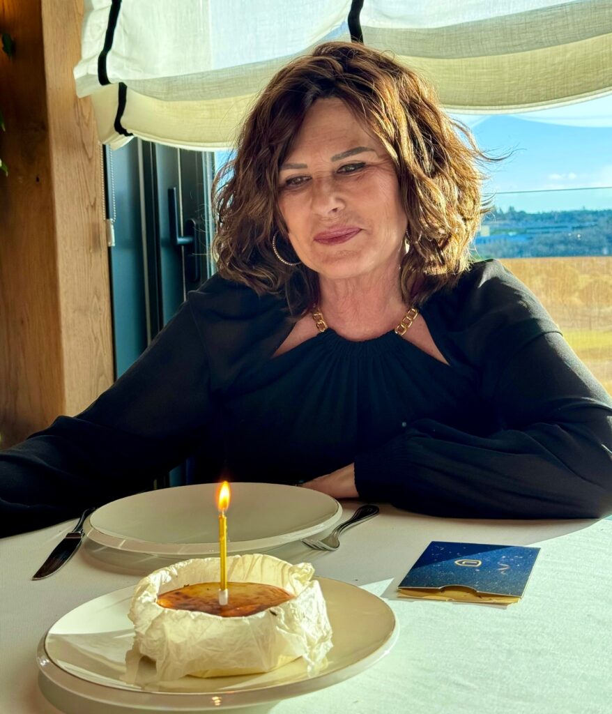 A woman with a square face shape sits at a table with a small birthday cake, sporting a voluminous, shoulder-length brunette bob with a tousled, wavy texture.