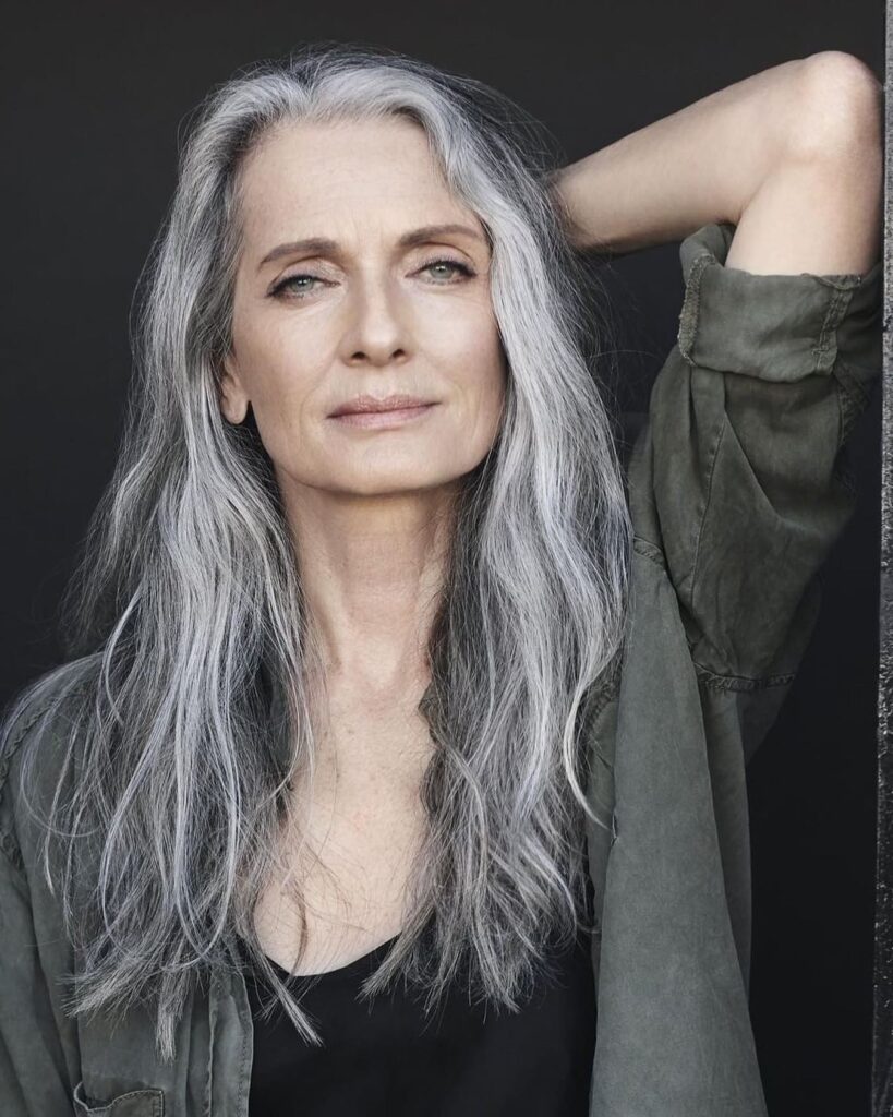 A woman over sixty with a square face shape, wearing long, flowing silver hair with soft waves and subtle layers.