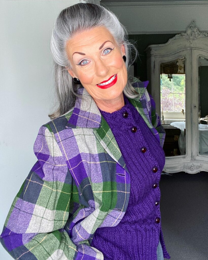 A woman over sixty with a square face shape wearing a shoulder-length silver hairstyle that is swept back with volume at the crown.