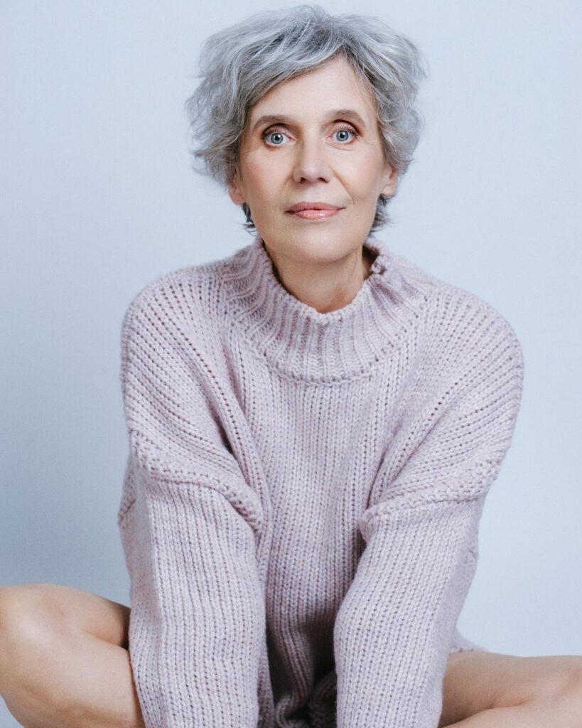 A woman over sixty with a square face shape wearing a short silver pixie cut with natural soft curls and volume on top.