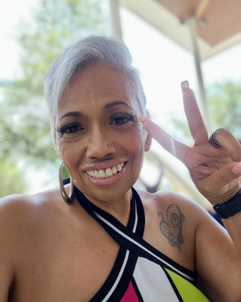A smiling woman over 60 with a modern side-swept silver pixie cut featuring short sides and a longer textured top.