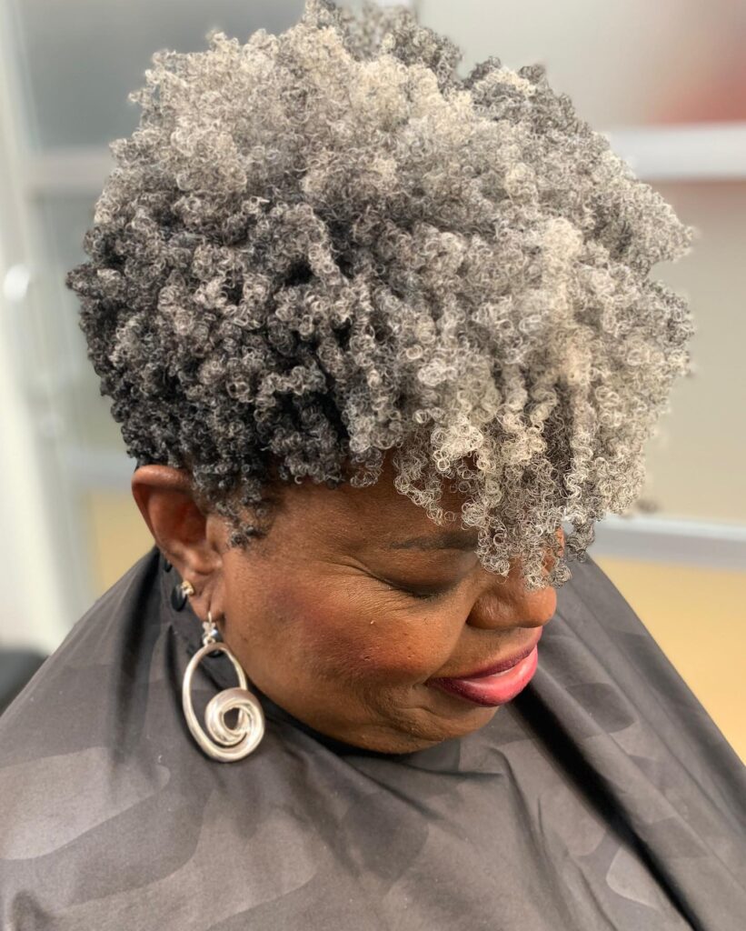 A woman with a stylish salt-and-pepper frohawk featuring short sides and voluminous silver curls styled toward the front.
