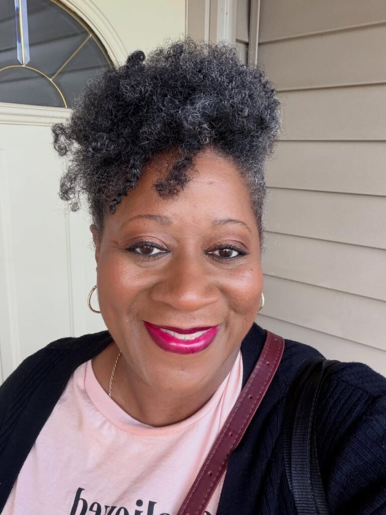 A smiling woman with a salt-and-pepper curly faux hawk hairstyle featuring textured height and a soft fringe.