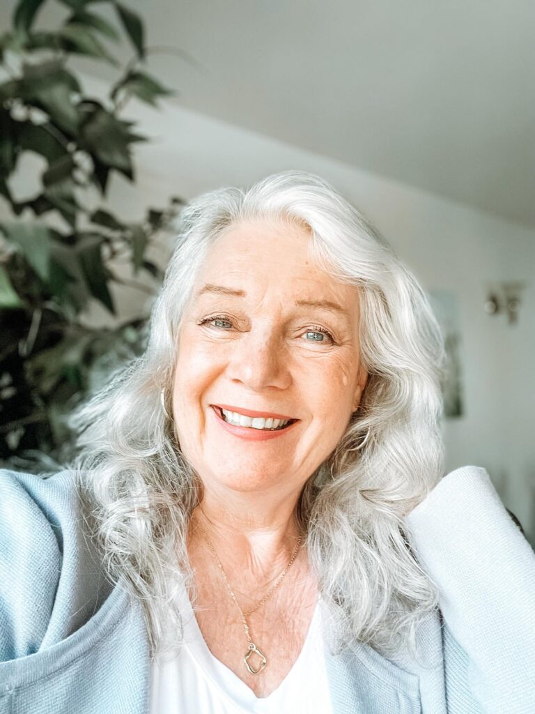 A woman with a round face wearing a medium-length silver wavy haircut with long layers and a side part.
