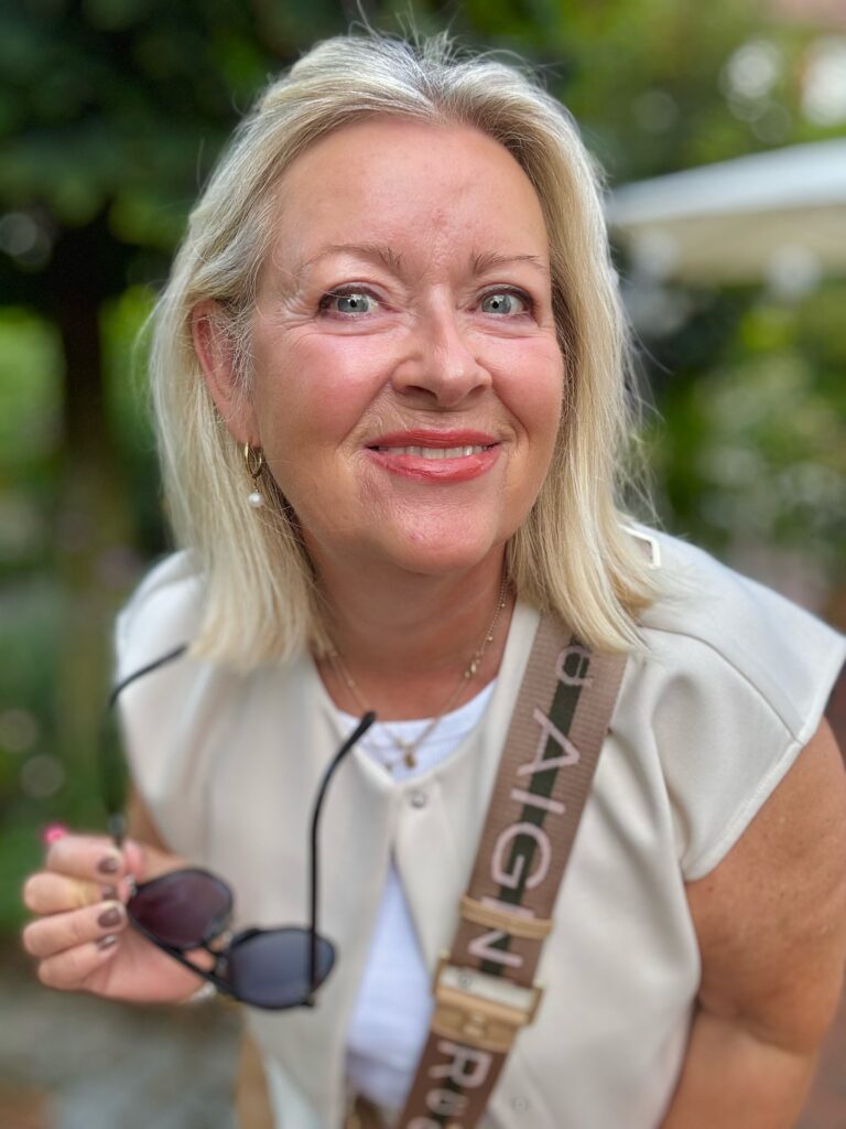 A woman with a round face wearing a sleek, medium-length, vanilla blonde lob with blunt ends and a swept-back style.