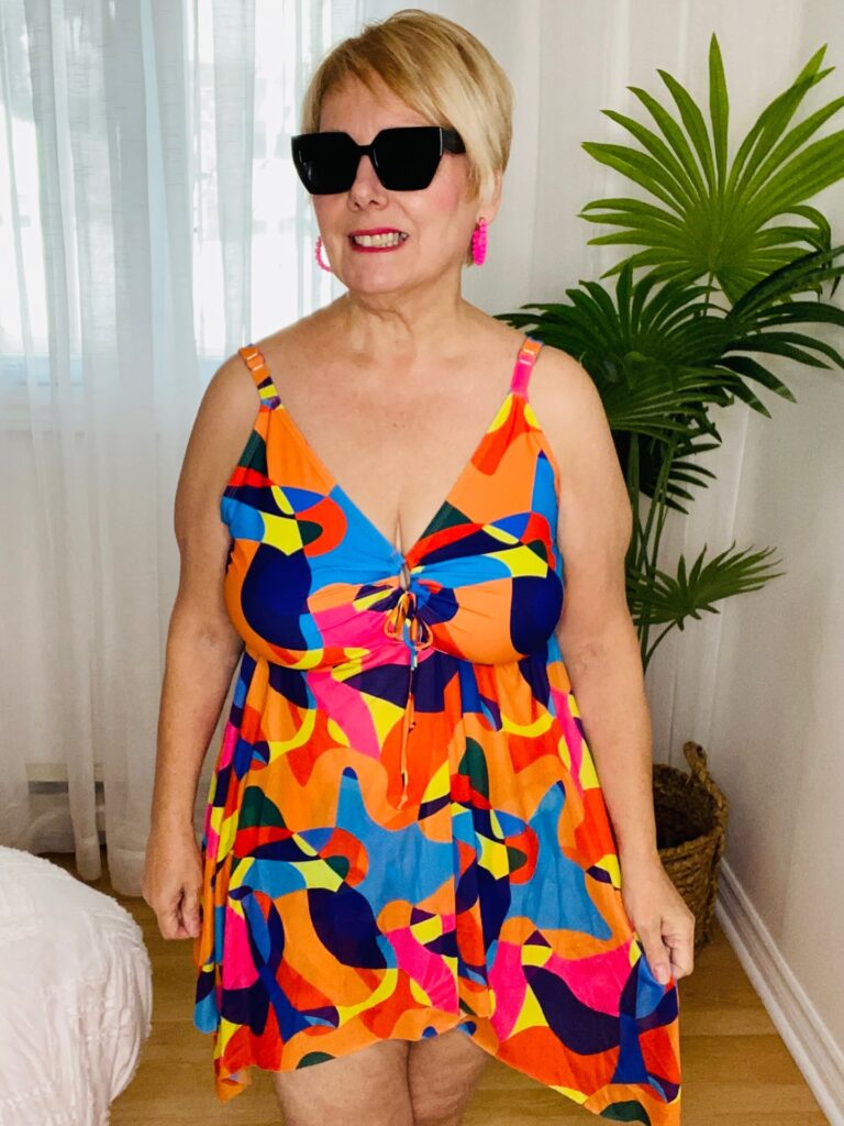 A woman over 60 wearing sunglasses and a colorful dress with a short honey-blonde pixie haircut.