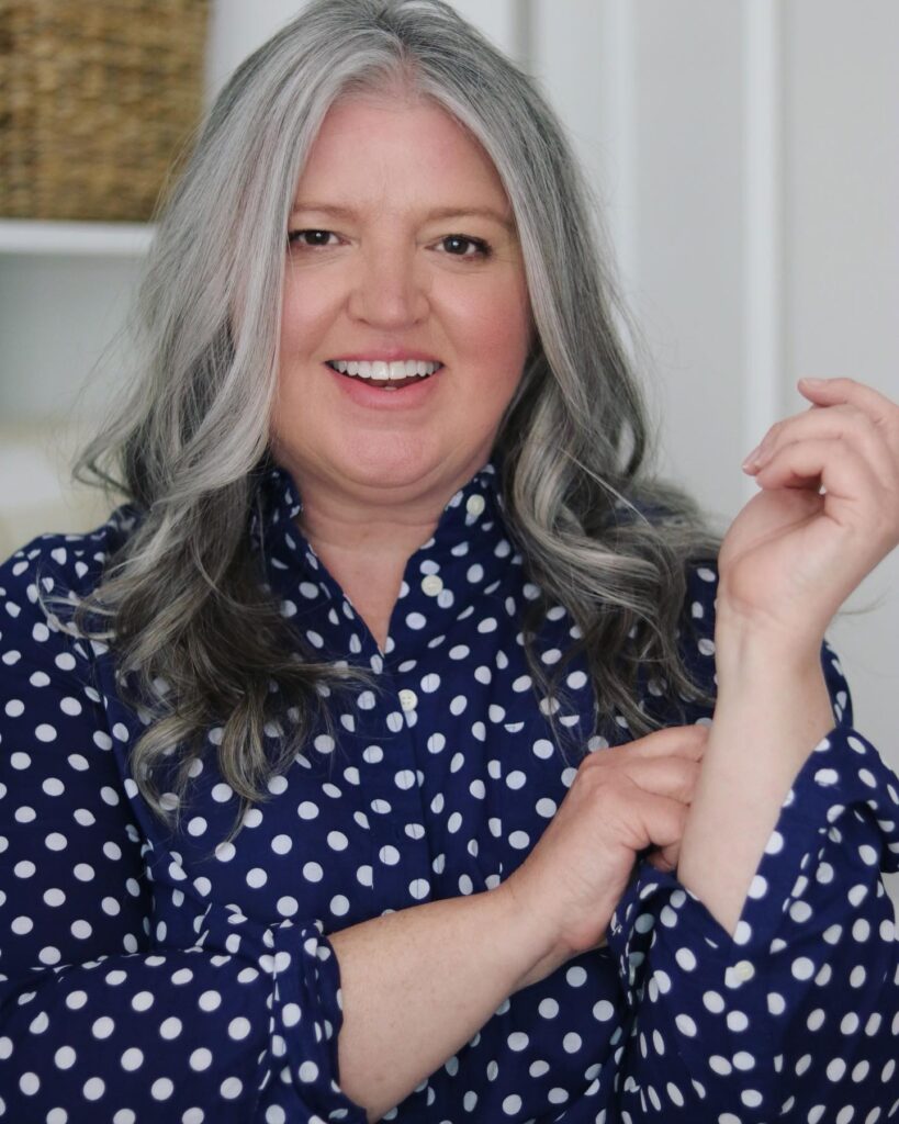 A woman over 60 with long, wavy salt and pepper hair styled with a center part.