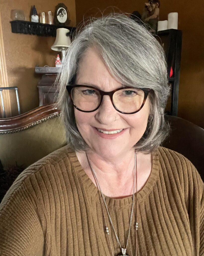 A woman over 60 with a chic silver chin-length bob and side-swept volume wearing glasses and a brown sweater.