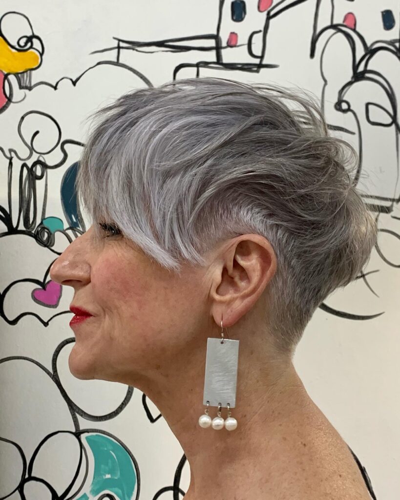 Short silver pixie haircut with an undercut and side-swept layers.
