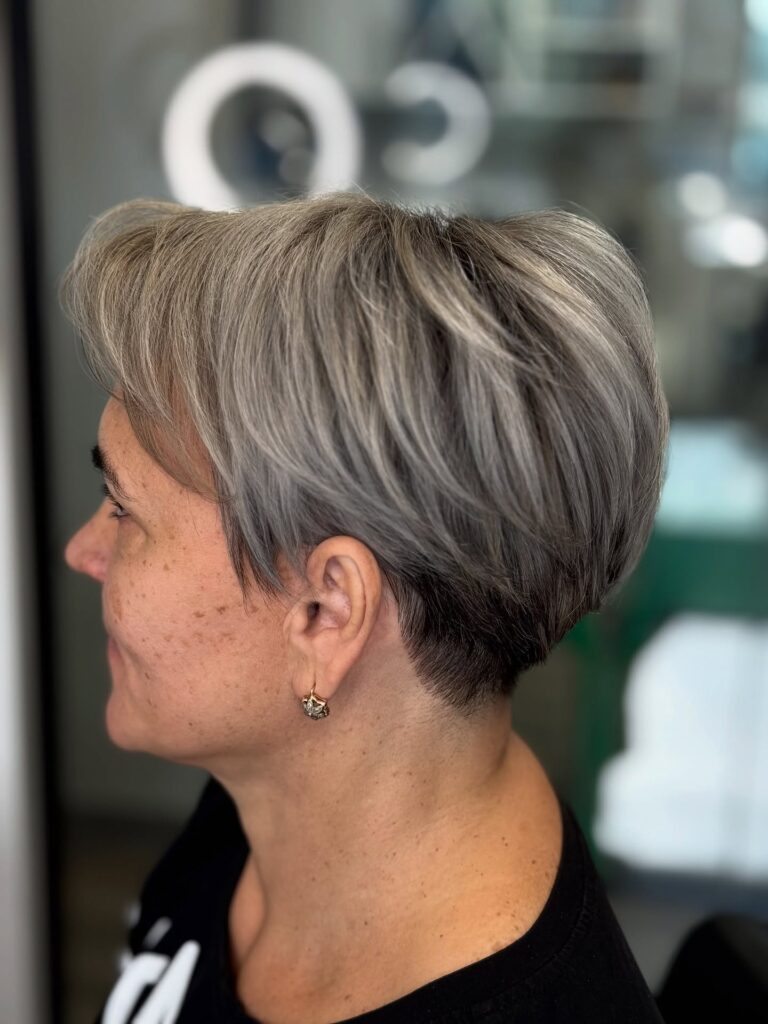 Short gray pixie haircut with a side part and a tapered back.