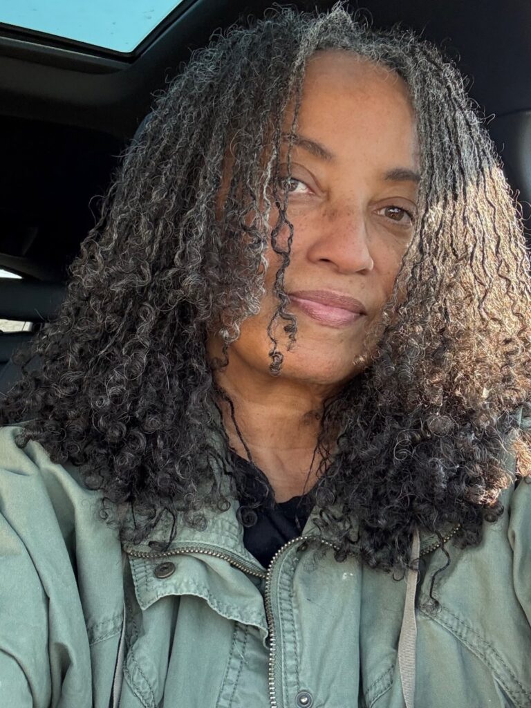 A woman with shoulder-length silver-and-black sisterlocks featuring curled ends and a center part.