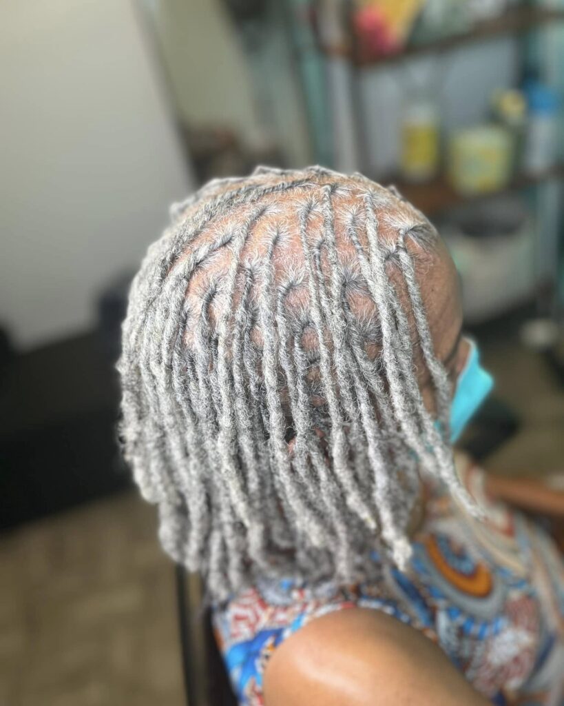 A top-down view of a woman over 60 with neatly partitioned medium-length silver locs.