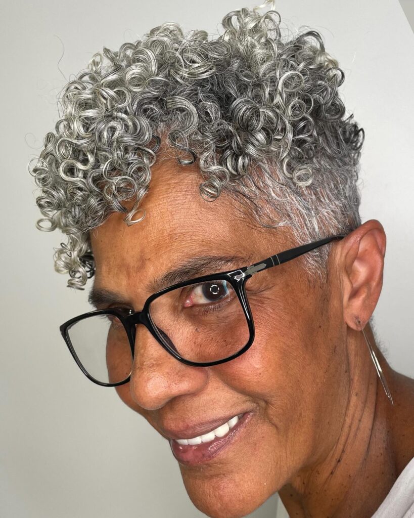 A close-up of a woman over 60 with a silver-and-black natural curly faux hawk hairstyle.