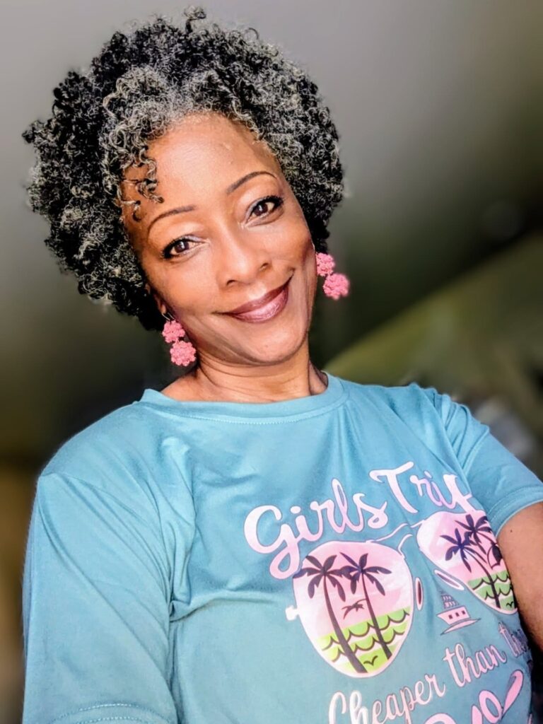 A woman over 60 with a short, rounded, natural hairstyle featuring dark, tight coils and silver highlights at the front.