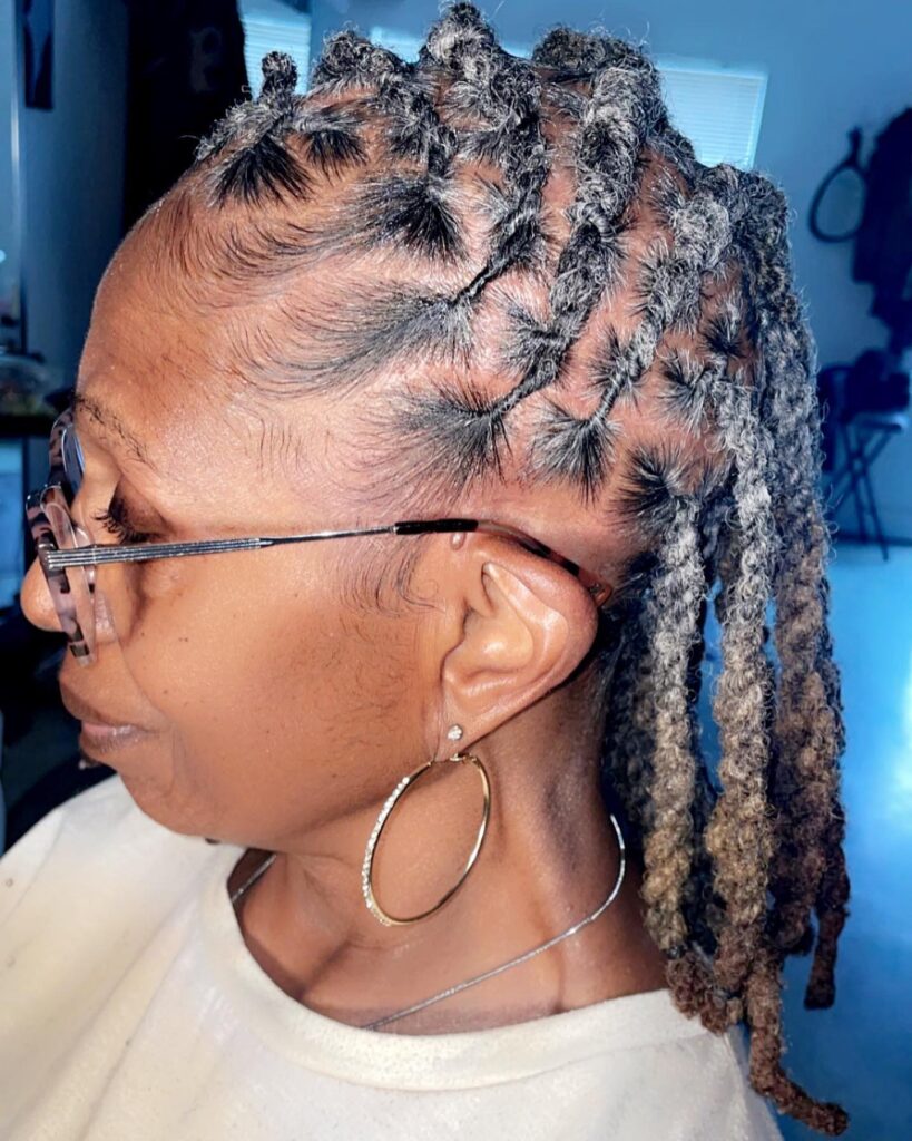 A side profile of a woman over 60 with segmented natural silver locs styled in neat sections along the scalp.